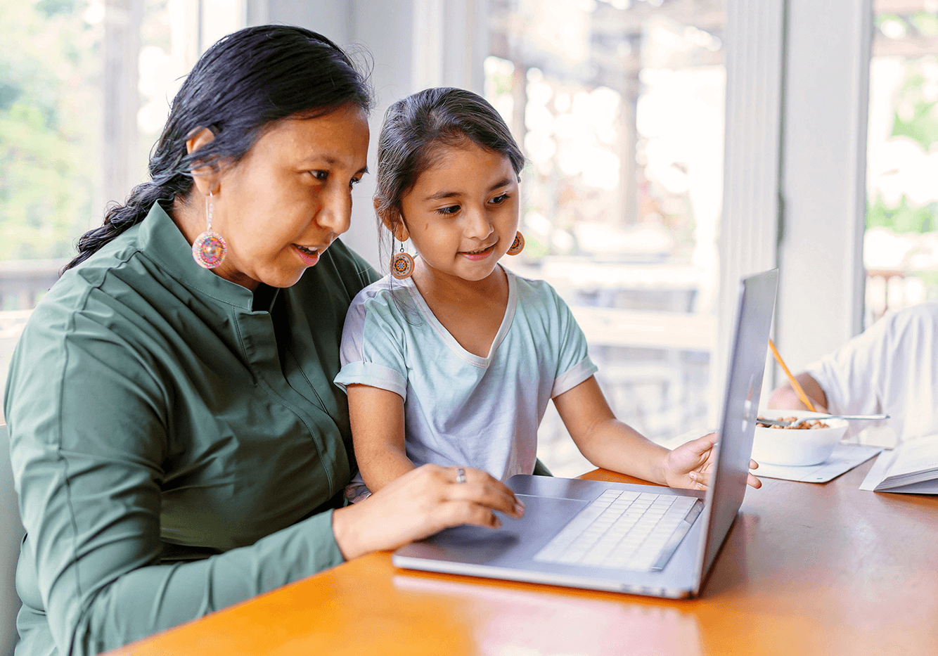 Woman and child sitting at a table looking at a laptop.